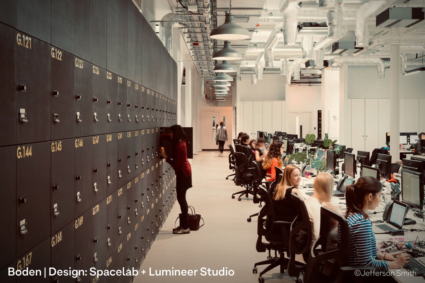 Architectural pendant lights inside Boden's open plan UK office, lighting co-working desks, lockers and seating areas