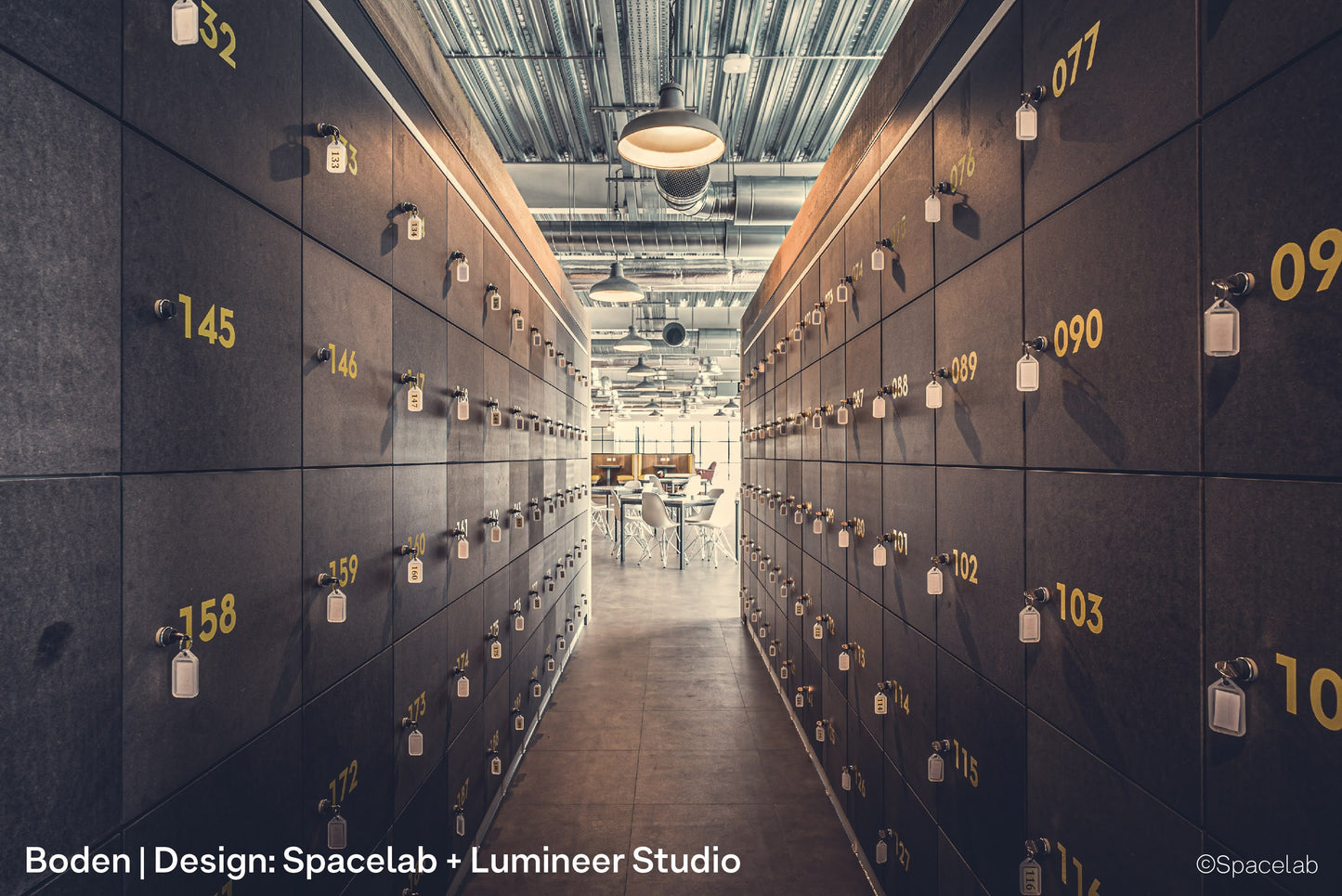 Architectural pendant lights inside Boden's open plan UK office, lighting co-working desks, lockers and seating areas