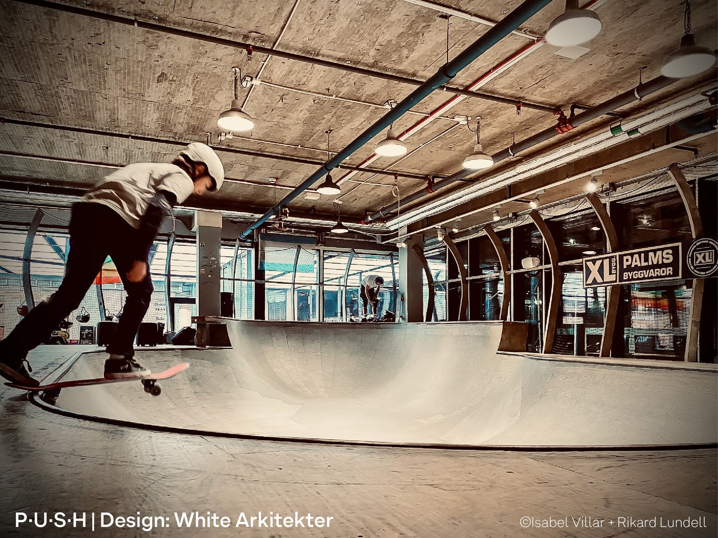 Skateboarders, skating at an indoor skatepark, illuminated by high-output architectural pendant lights