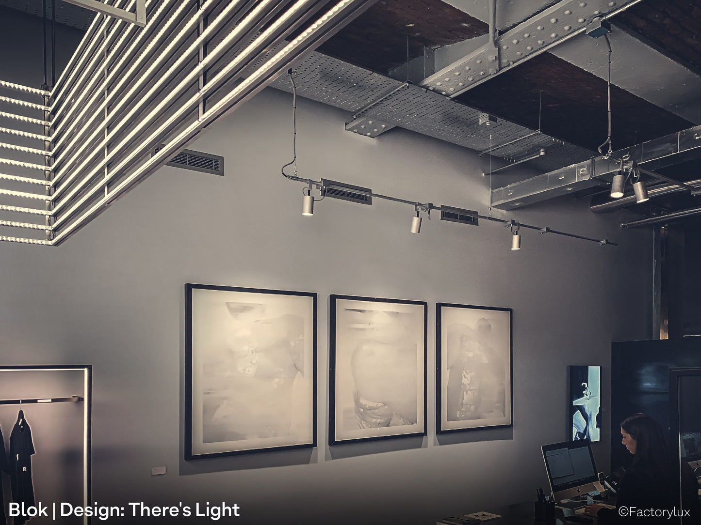 Raw aluminium architectural spotlights, ceiling mounted on steel conduit tubes to light paintings in an art gallery 